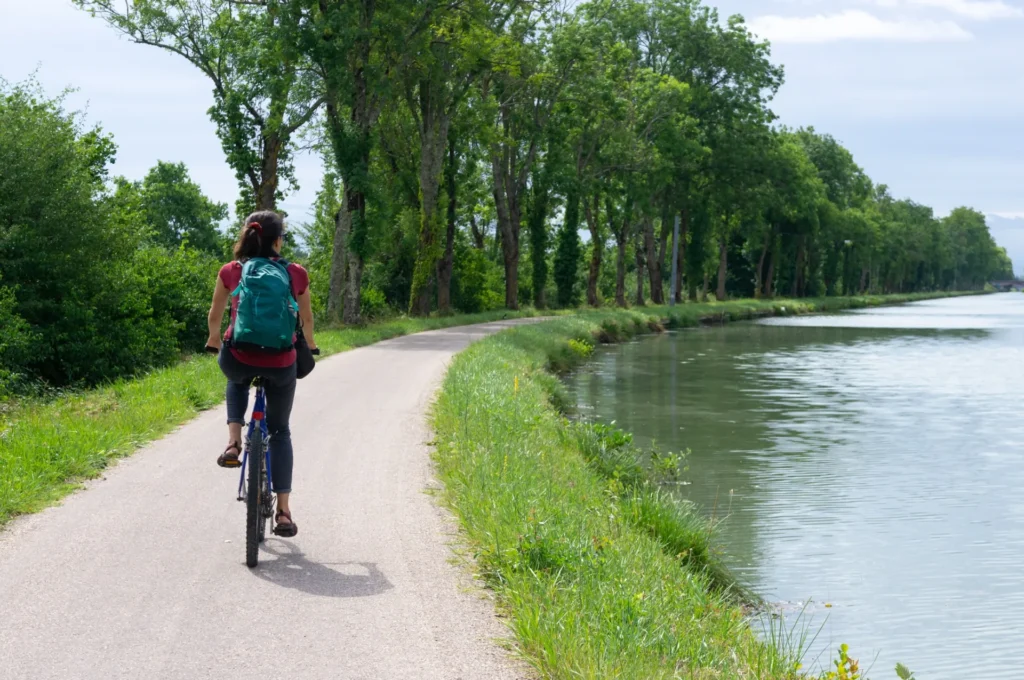 Cycliste se promenant à vélo sur un chemin au bord d’un canal entouré d’arbres